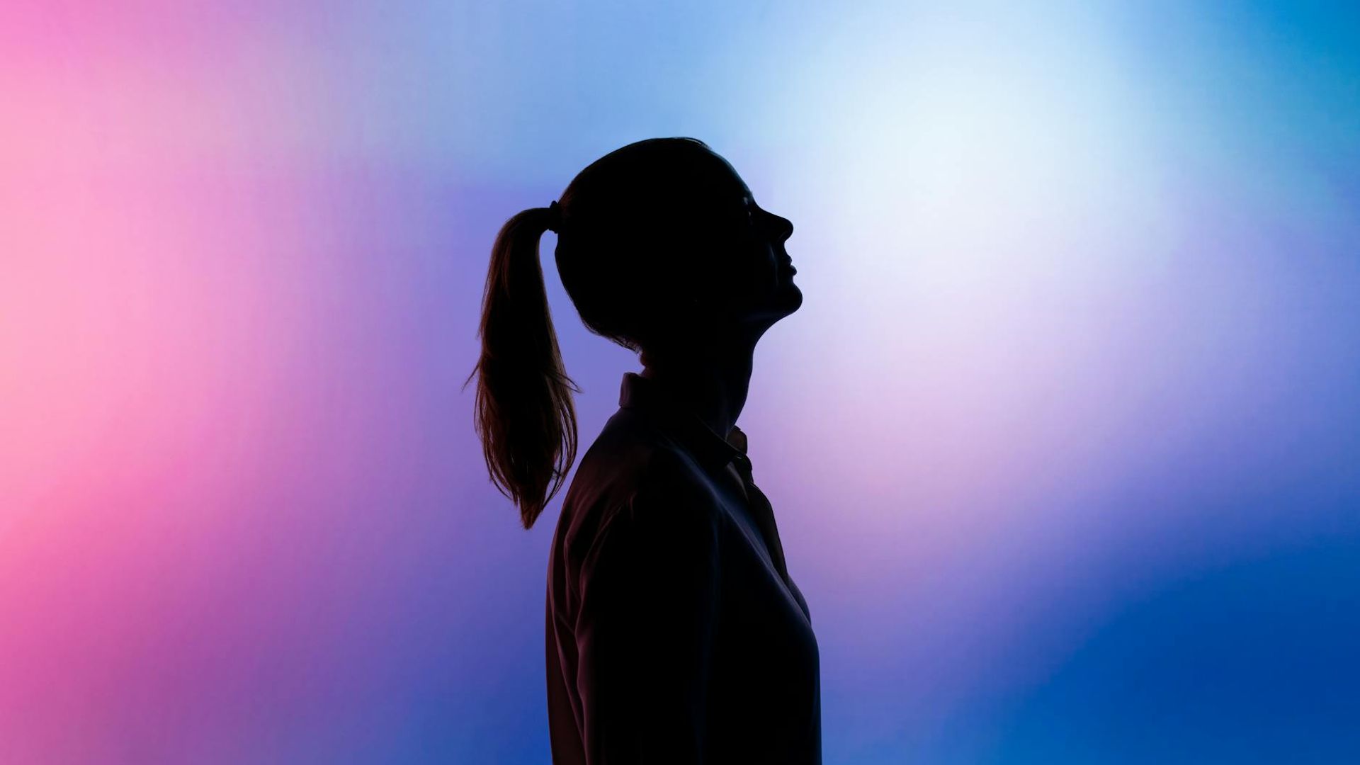 Silhouette of a woman in a calm yoga pose against a soft, dark background.